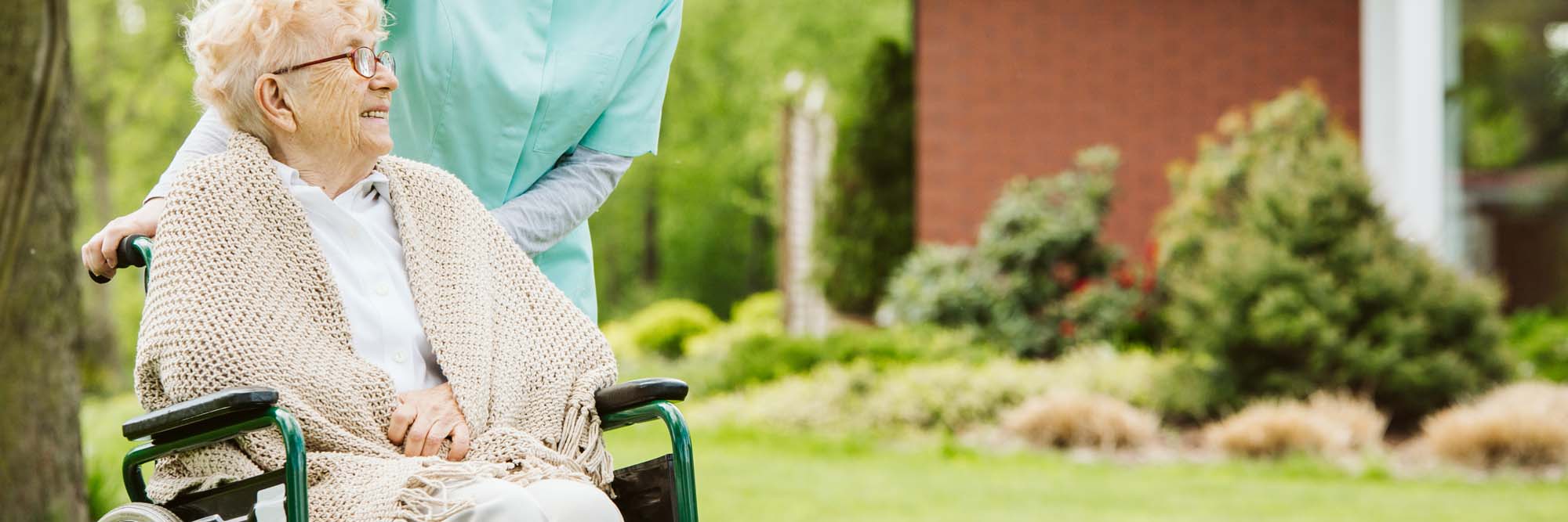 Senior disabled woman with caregiver in the garden of the nursing home